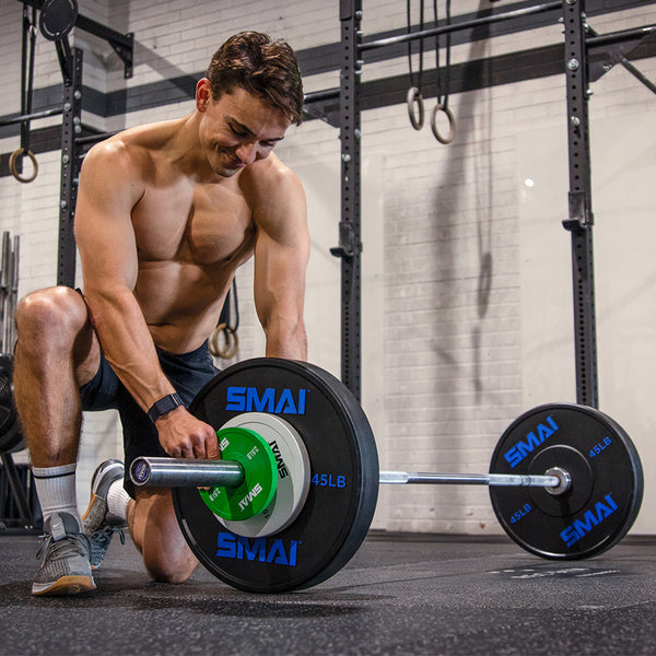 Man loading up a Barbell with 45LB SMAI Bumper Plates